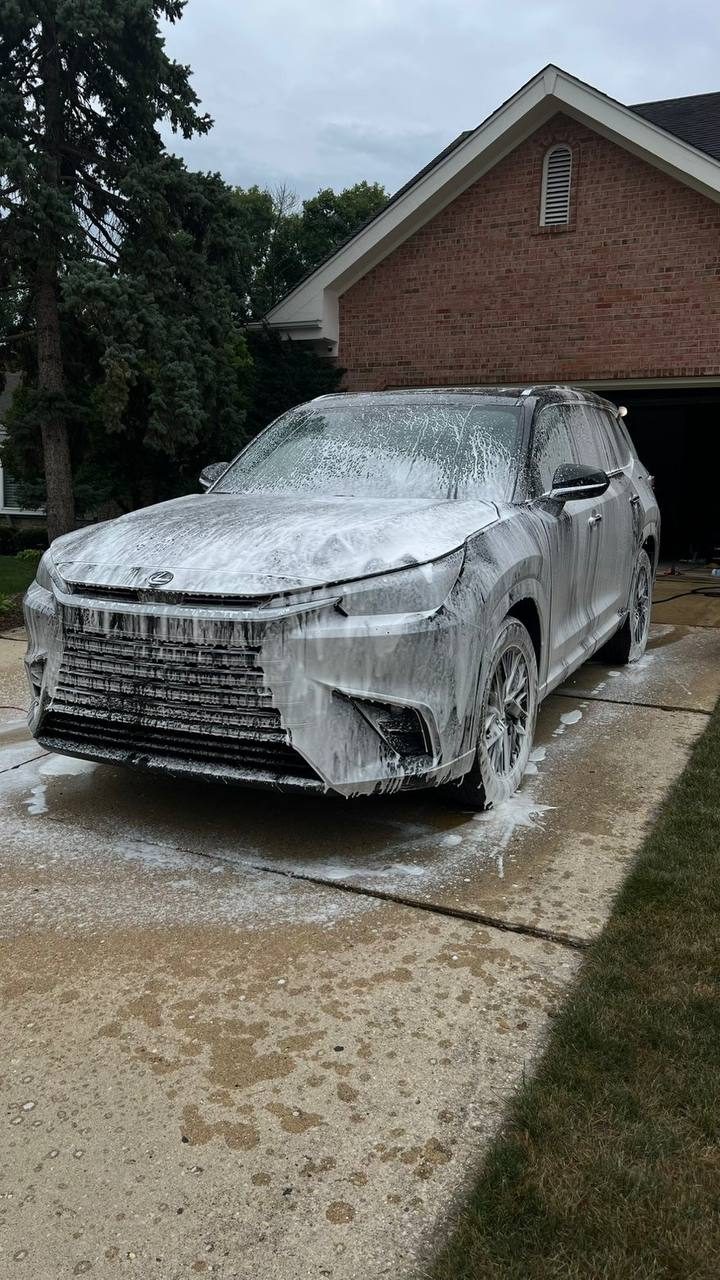 Lexus SUV covered in foam during a pre-wash in a driveway